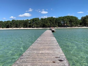 A wooden pier extending into clear water with a boat docked at the end, surrounded by a forested shoreline.