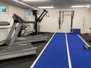 Ein Fitnessraum mit Laufband, Trainingsgeräten und einer blauen Matte.