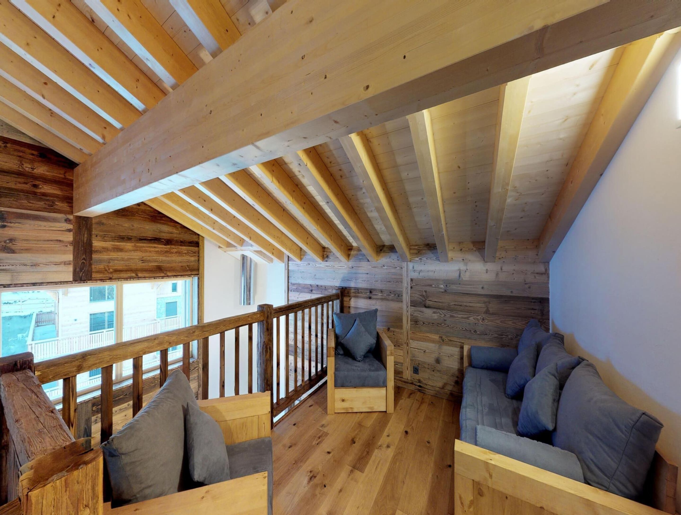 A cozy attic room with wooden beams, a wooden railing, and two sofas with cushions.