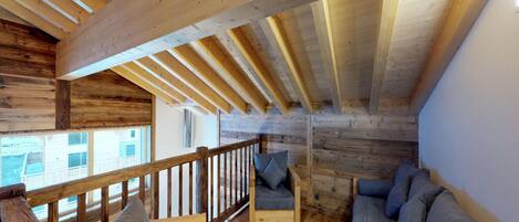 A cozy attic room with wooden beams, a wooden railing, and two sofas with cushions.