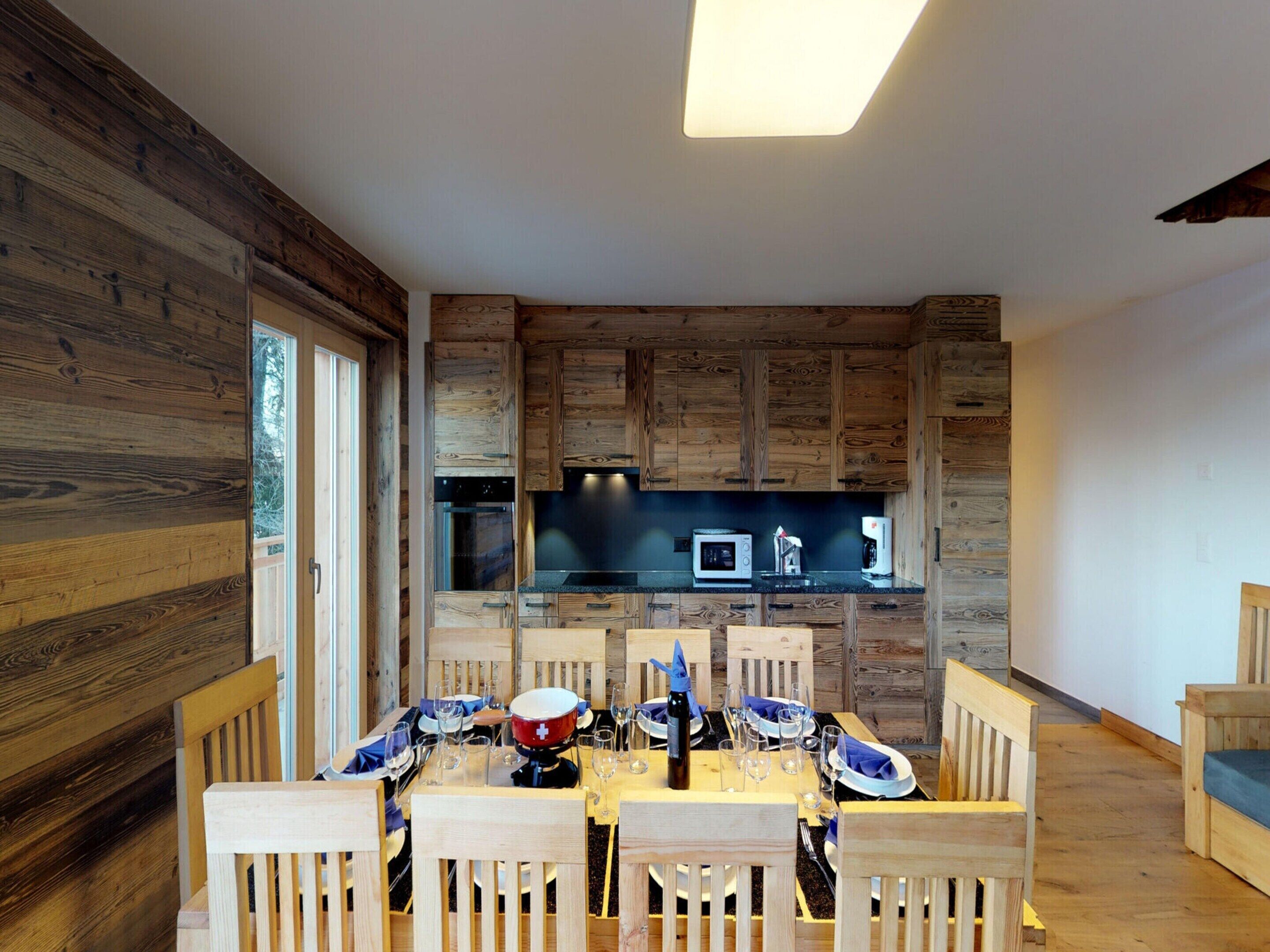 A dining area with wooden walls and a modern kitchen in the background.