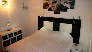 Un dormitorio con una cama, mesitas de noche, una lámpara de pared y un cuadro.