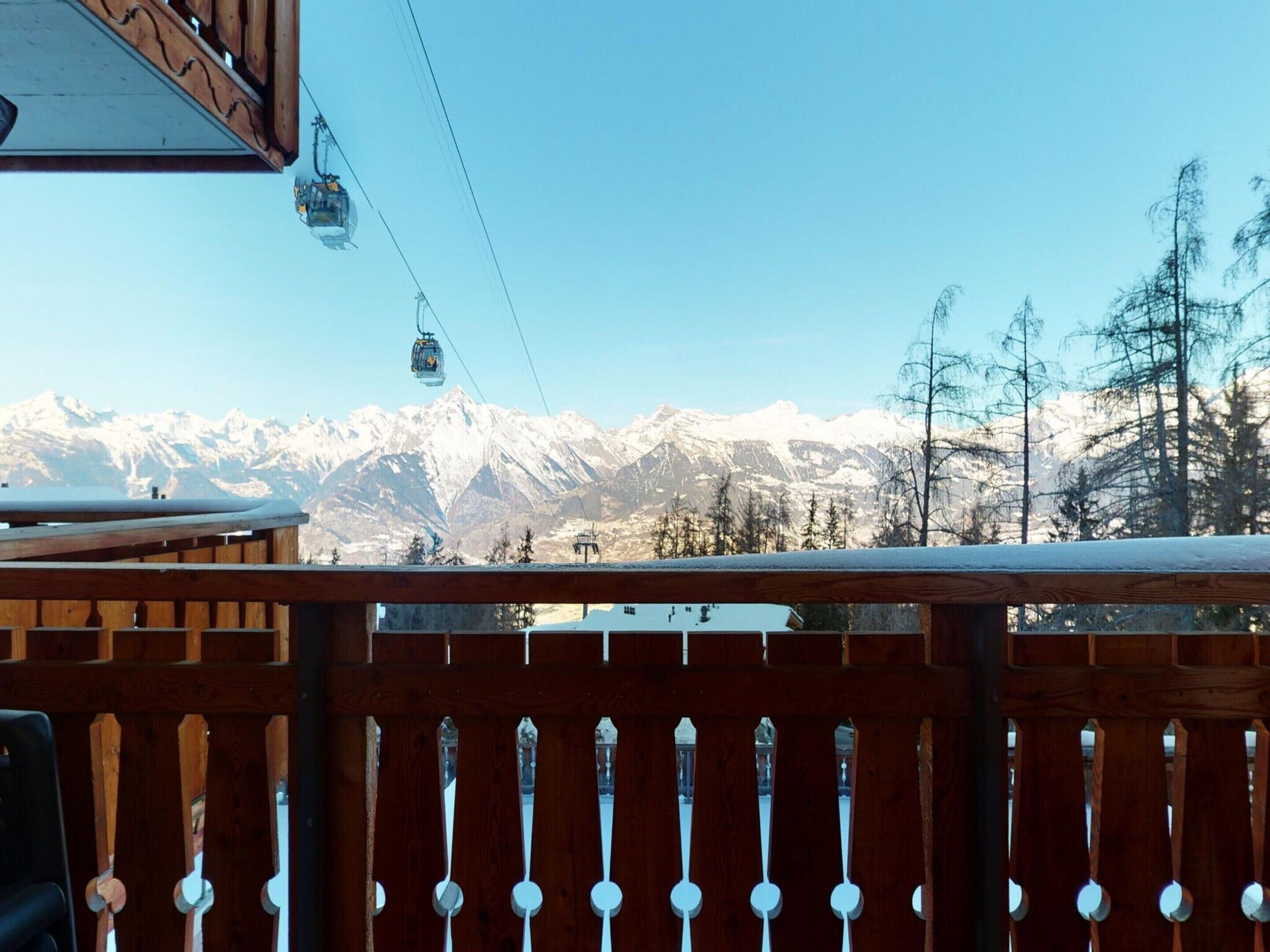 A wooden deck with a view of snow-covered mountains and a ski lift in the background.