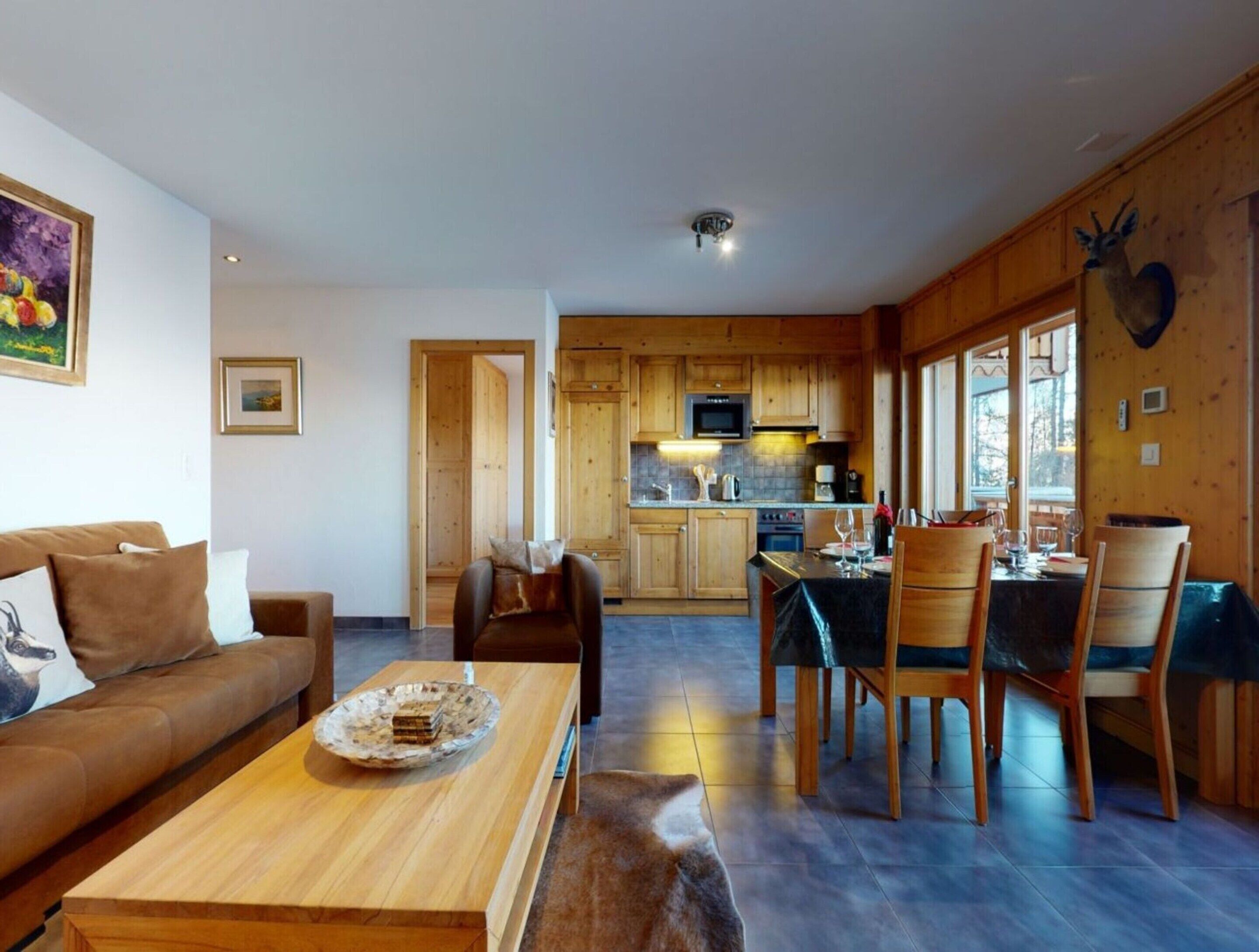 Un salon chaleureux avec un canapé en bois, une table à manger avec des chaises, et une cuisine en arrière-plan.