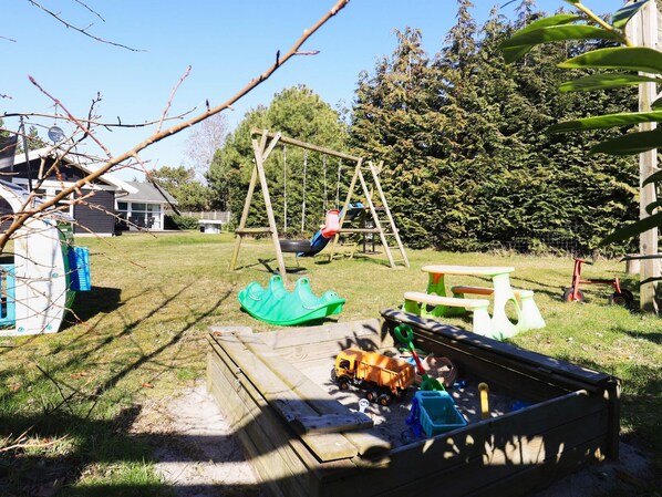 Un jardin avec une balançoire, un bac à sable et une petite maison de jeu.