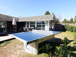 An outdoor ping pong table with a white table and blue playing surface, surrounded by a patio area with chairs and a table. - 4 Star Holiday Home in Vaeggerlose (Vaeggerlose)