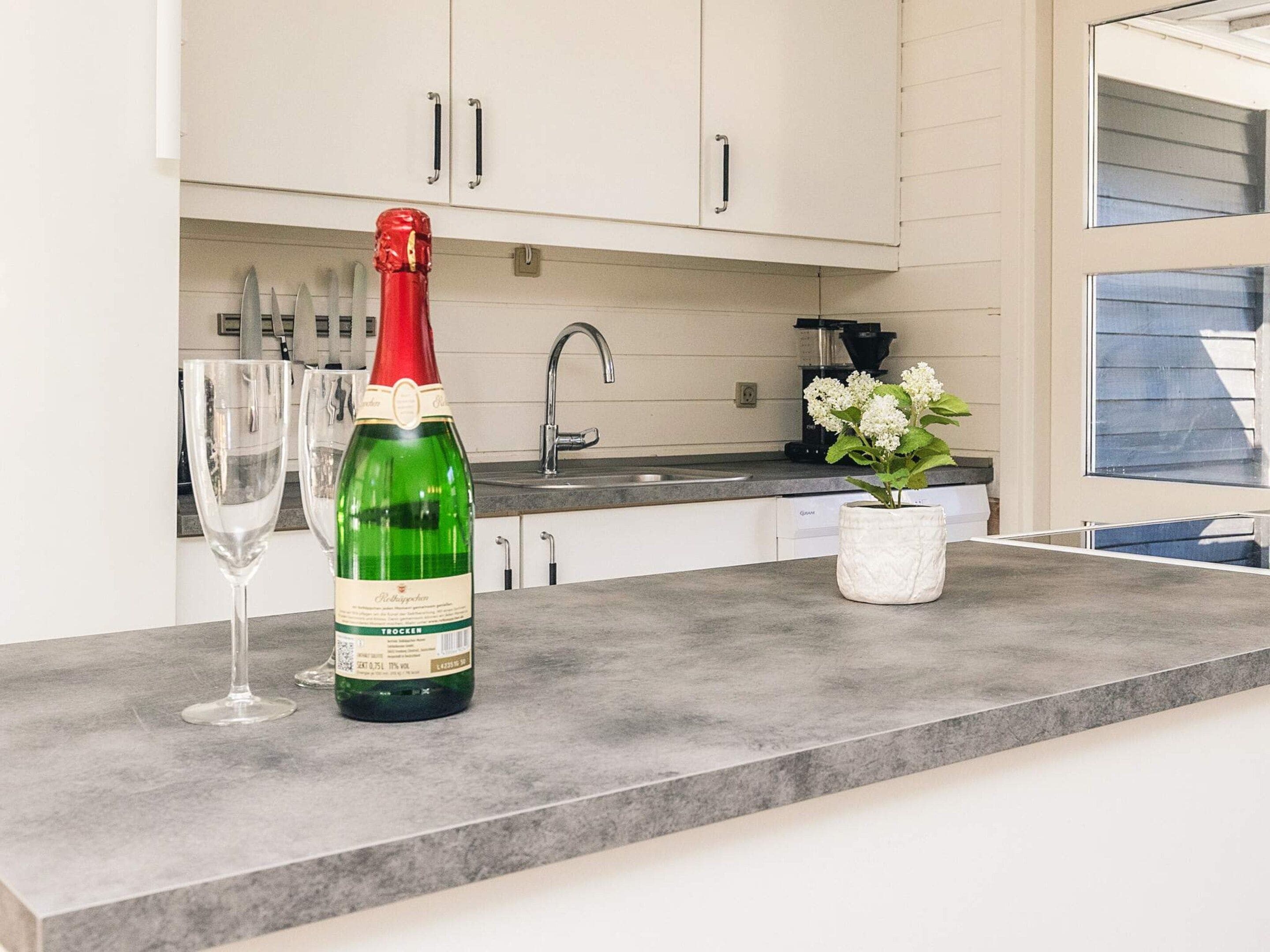 A kitchen with a countertop, a bottle of wine, and a vase with flowers.