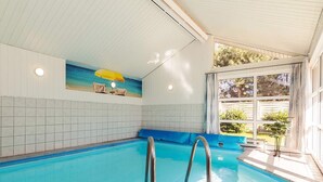 Una piscina interior con agua azul cristalina, suelo de baldosas y un mural con escena de playa en la pared.
