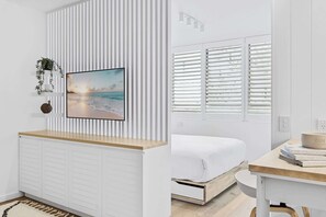 Une chambre moderne avec un lit, un bureau et une grande fenêtre équipée de stores.