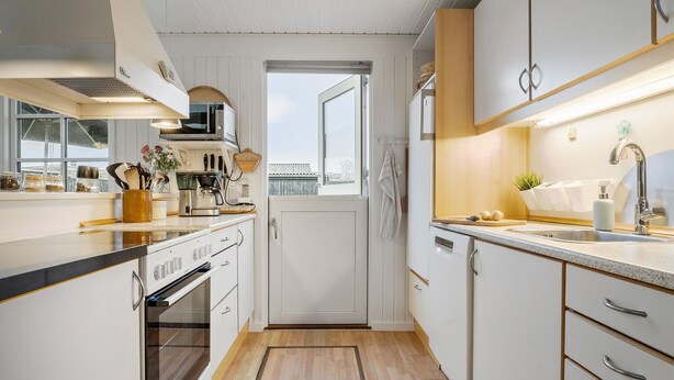 Una cucina ristretta con forno a incasso, microonde e macchina del caffè. Si vede una finestra con vista su un edificio.