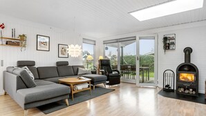 Un soggiorno moderno con un divano angolare grigio, un tavolino in legno e una poltrona in pelle nera. È presente un camino con legna e canna fumaria, e un'ampia finestra con vista su un giardino.