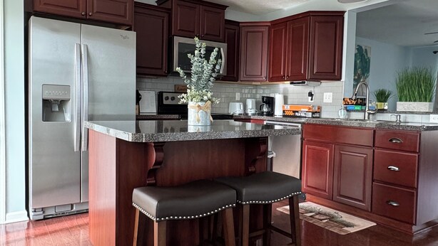 A kitchen with a central island, dark wooden cabinets, stainless steel appliances, and a potted plant.
