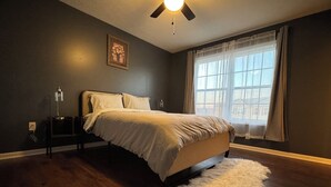 A bedroom with a bed, a ceiling fan, a window with curtains, and a small rug.