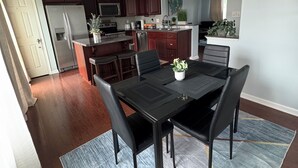 A modern kitchen with dark wood cabinets, a stainless steel refrigerator, and a dining area with a black table and chairs.