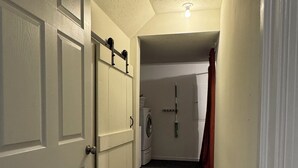 A hallway with a carpeted floor, white walls, and a laundry area with a washing machine and a drying rack.