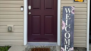 A dark red door with a window, a welcome sign, and a doormat.