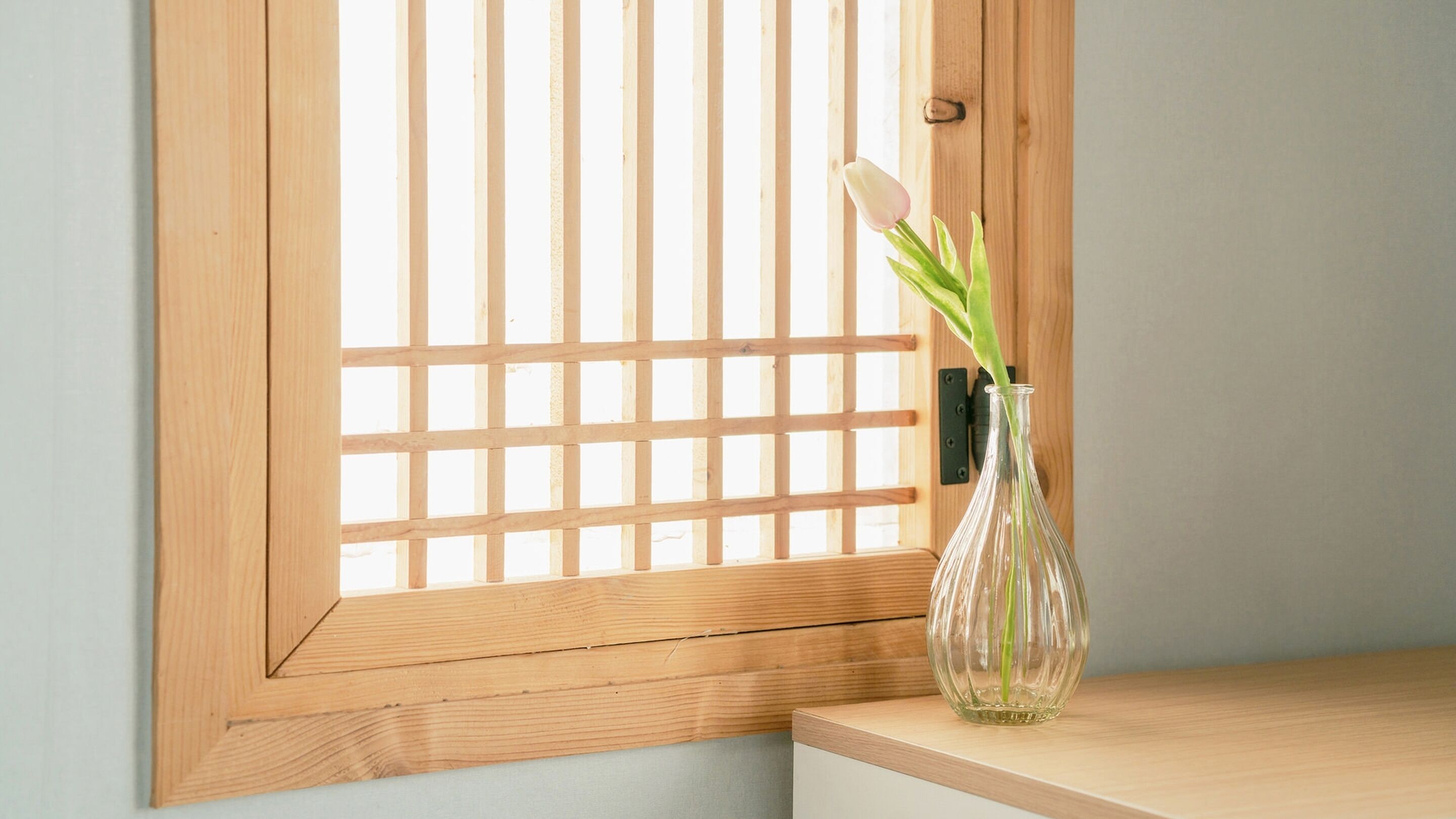 A wooden door with a grid pattern, a clear glass vase with a green plant on a wooden ledge.
