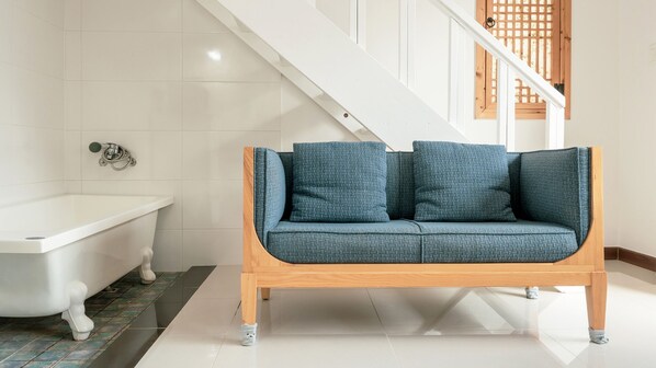 Een moderne badkamer met een wit bad, een houten bankje en een blauwe, beklede zitbank.