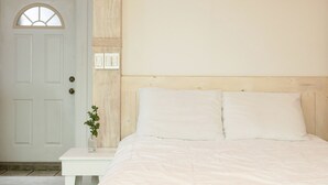 A bedroom with a white door, a small bedside table with a vase, and a bed with white bedding. - Gangreung Comichi Bada Pension (Gangneung)