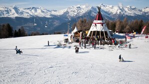 Ein verschneiter Skipisten mit einer großen Menschenmenge um eine tipiähnliche Konstruktion.