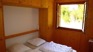 Ein kleines Zimmer aus Holz mit zwei Einzelbetten, einem Fenster mit Blick auf Grünflächen und Holzwänden.