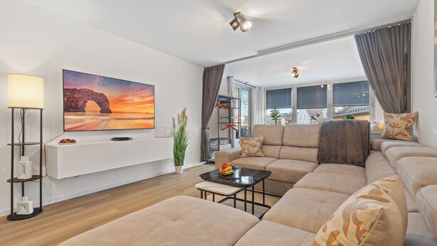 Una sala de estar moderna con un sofá grande, una mesa de centro, un televisor de pantalla plana y una lámpara de pie.