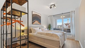 Un dormitorio con cama, una silla colgante, estante, lámpara y ventana con vista a una torre.