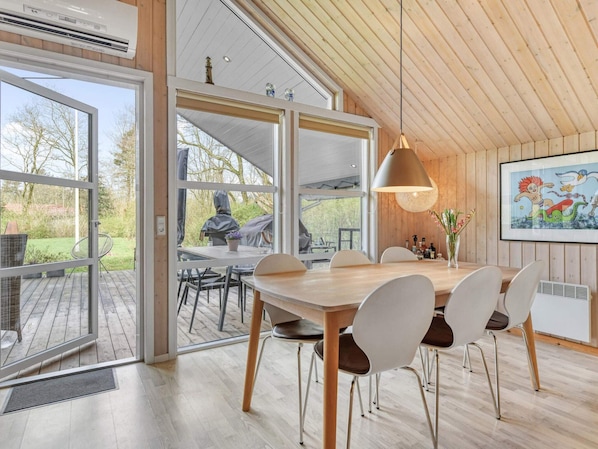 A dining area with a wooden table and chairs, a pendant light, and a view of the outdoors.