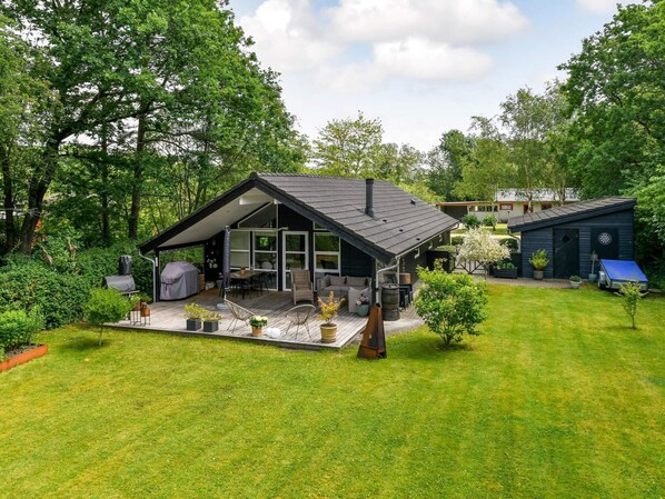 A modern house with a large deck, a barbecue area, and a small shed.
