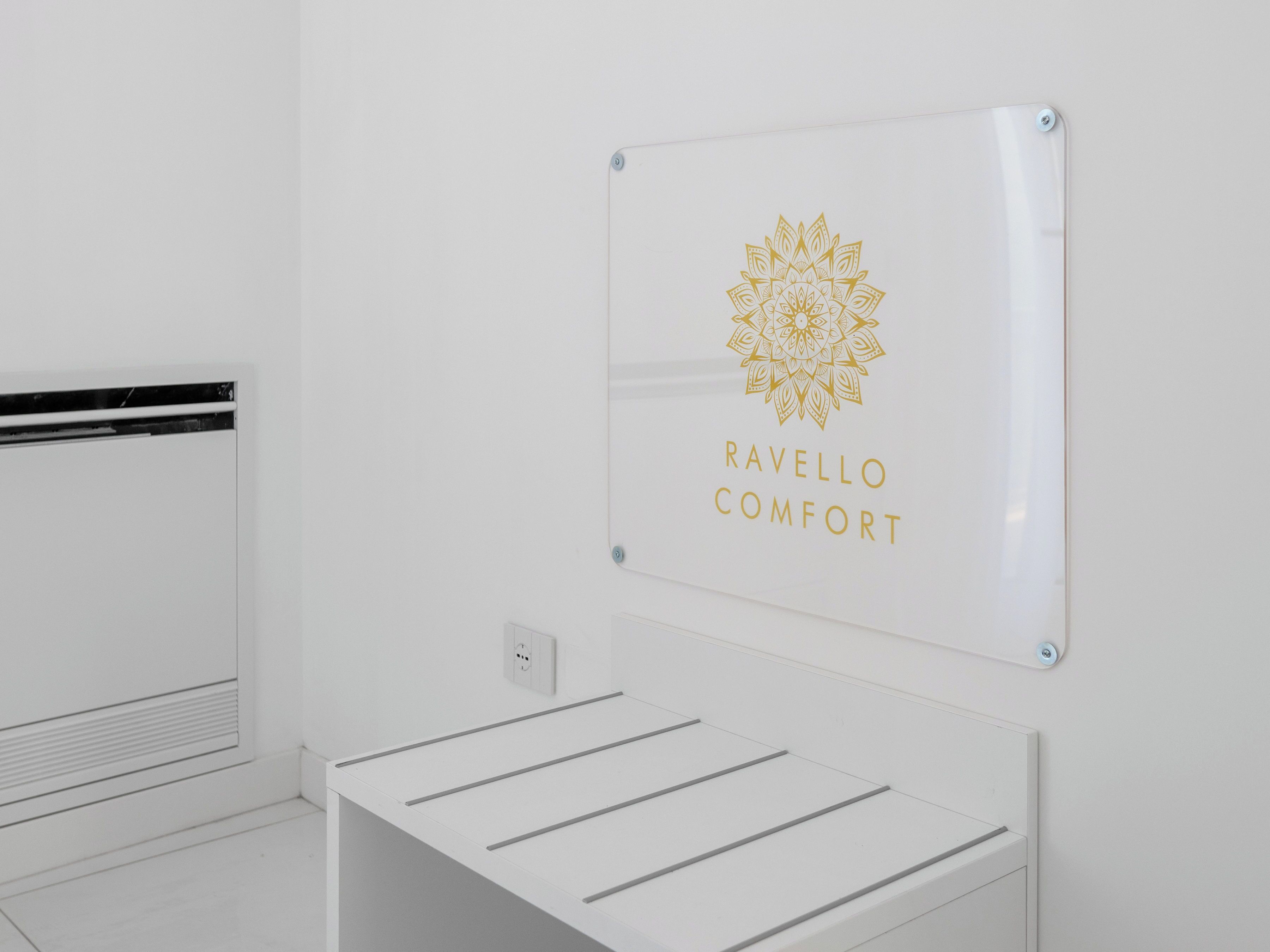 A white wall with a mounted sign featuring a mandala design and the text "RAVELLO COMFORT".