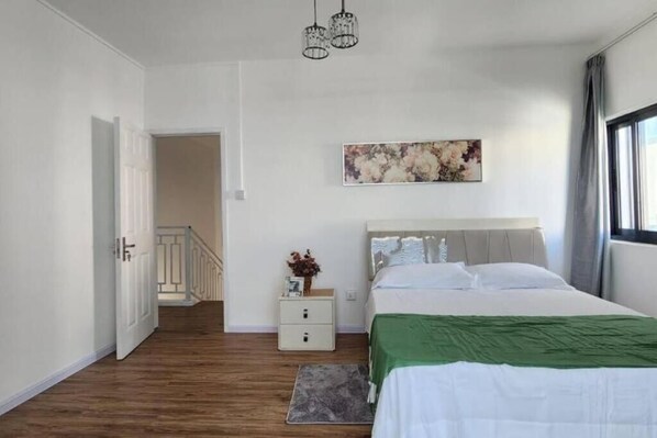 A bedroom with a bed, a nightstand, a painting, and a staircase.