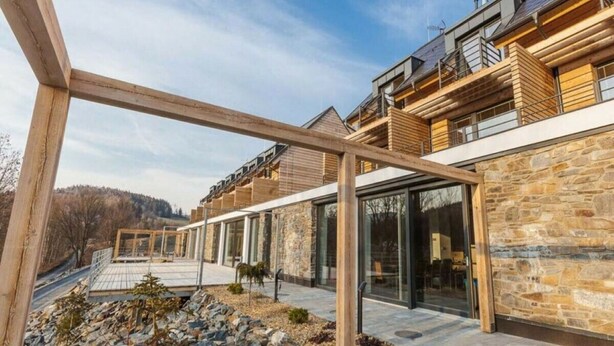 A modern building with a stone facade, large windows, and a wooden deck area. - Comfortable Villa With Pool (Mala Moravka)