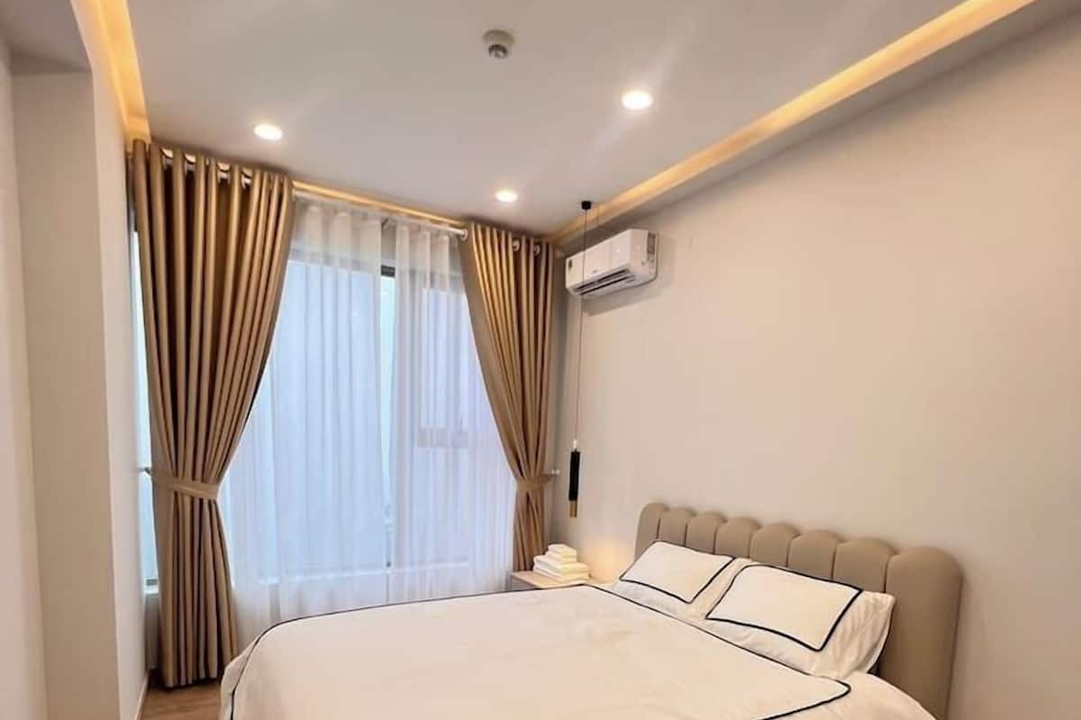 Un dormitorio moderno con una cama grande, una mesita de noche, un equipo de aire acondicionado y una ventana con cortinas.