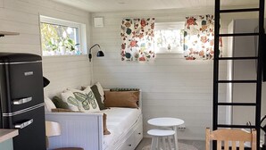 A compact room with a bed, a small table, a chair, a refrigerator, and a window with floral curtains. - 4 Person Holiday Home in Askloster (Åskloster)