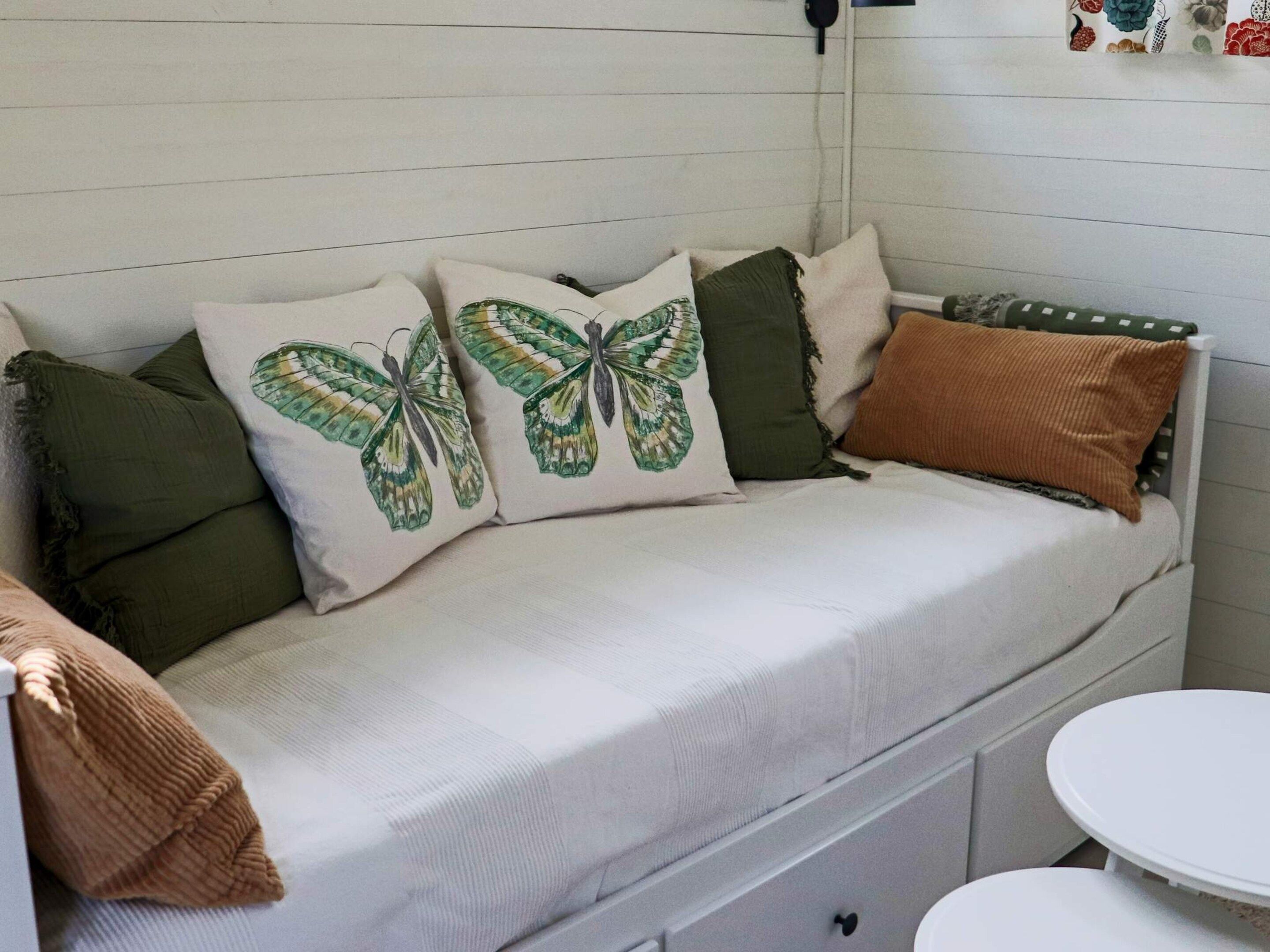 A white sofa with green and brown cushions, a small white table, and a wall with a floral pattern.