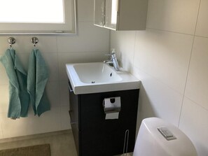 A bathroom with a white sink, a black cabinet, a toilet, and a towel rack with two towels. - 4 Person Holiday Home in Askloster (Åskloster)