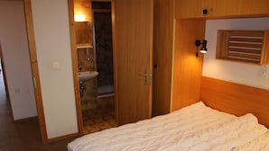 A bedroom with a bed, wooden wardrobe, and a bathroom visible through an open door. - Stunning Apartment With Mountain Views (Veysonnaz)