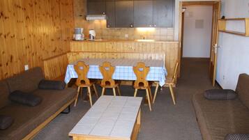A cozy room with a wooden wall, a dining table with chairs, a sofa, and a small table.
