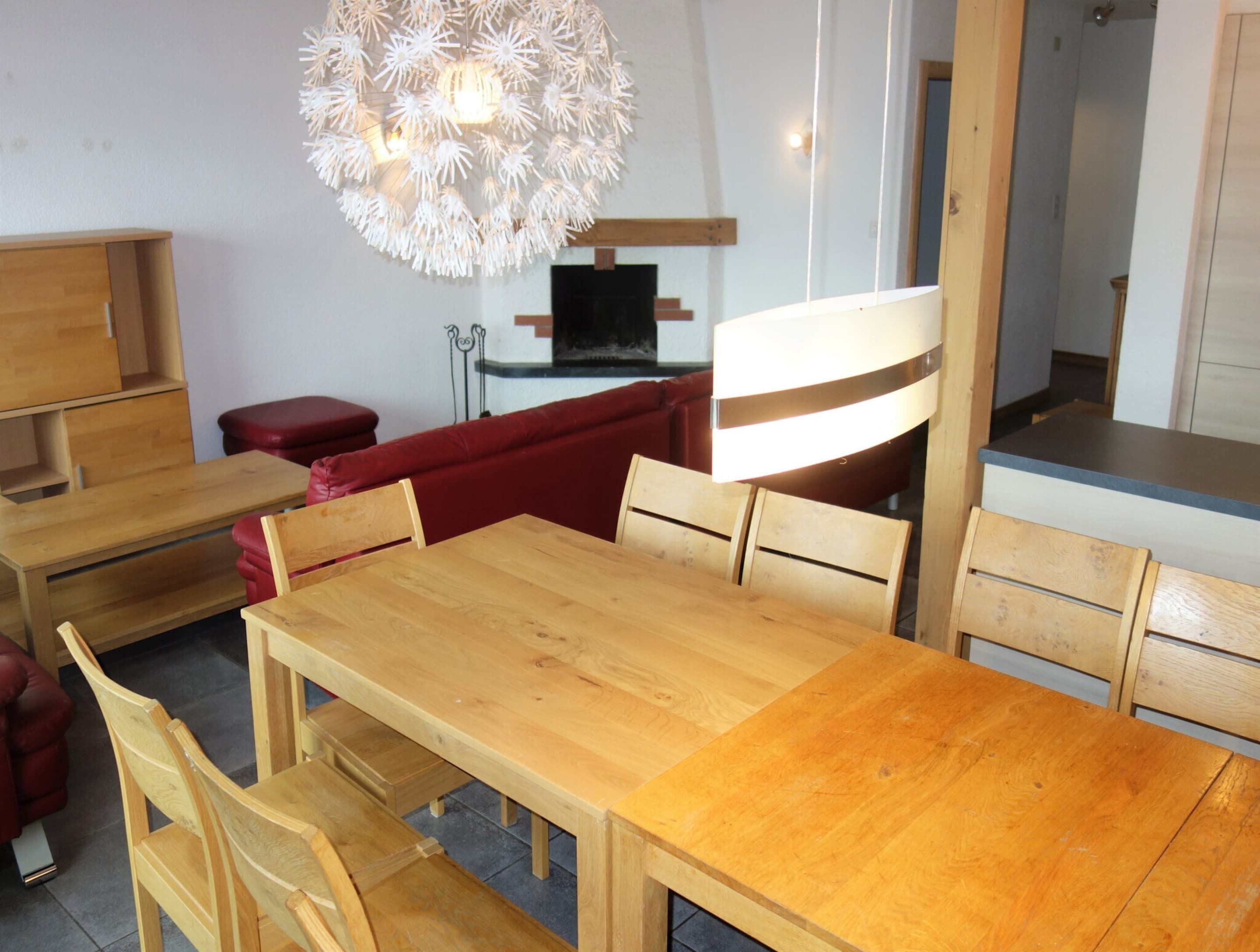 Ein moderner Essbereich mit Holztisch und -stühlen, einem roten Sofa und einem einzigartigen Kronleuchter.