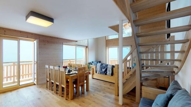 Ein großzügiger Wohnbereich mit einer Holztreppe, einem Esstisch mit Stühlen und einer Couch.