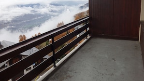 Ein Balkon mit Blick auf ein Tal und Berge, mit Holzgeländer und geschlossener Tür.