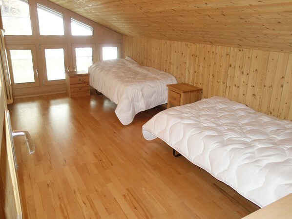 Une chambre avec deux lits, un plancher en bois et un plafond en pente doté de fenêtres.