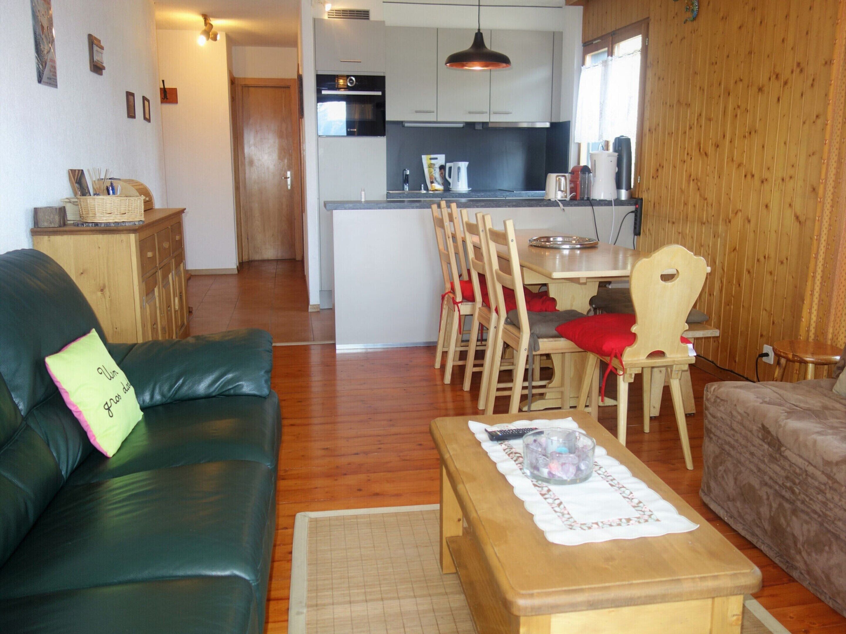 Un soggiorno con un divano verde, un tavolo da pranzo in legno e sedie, e una cucina sullo sfondo.