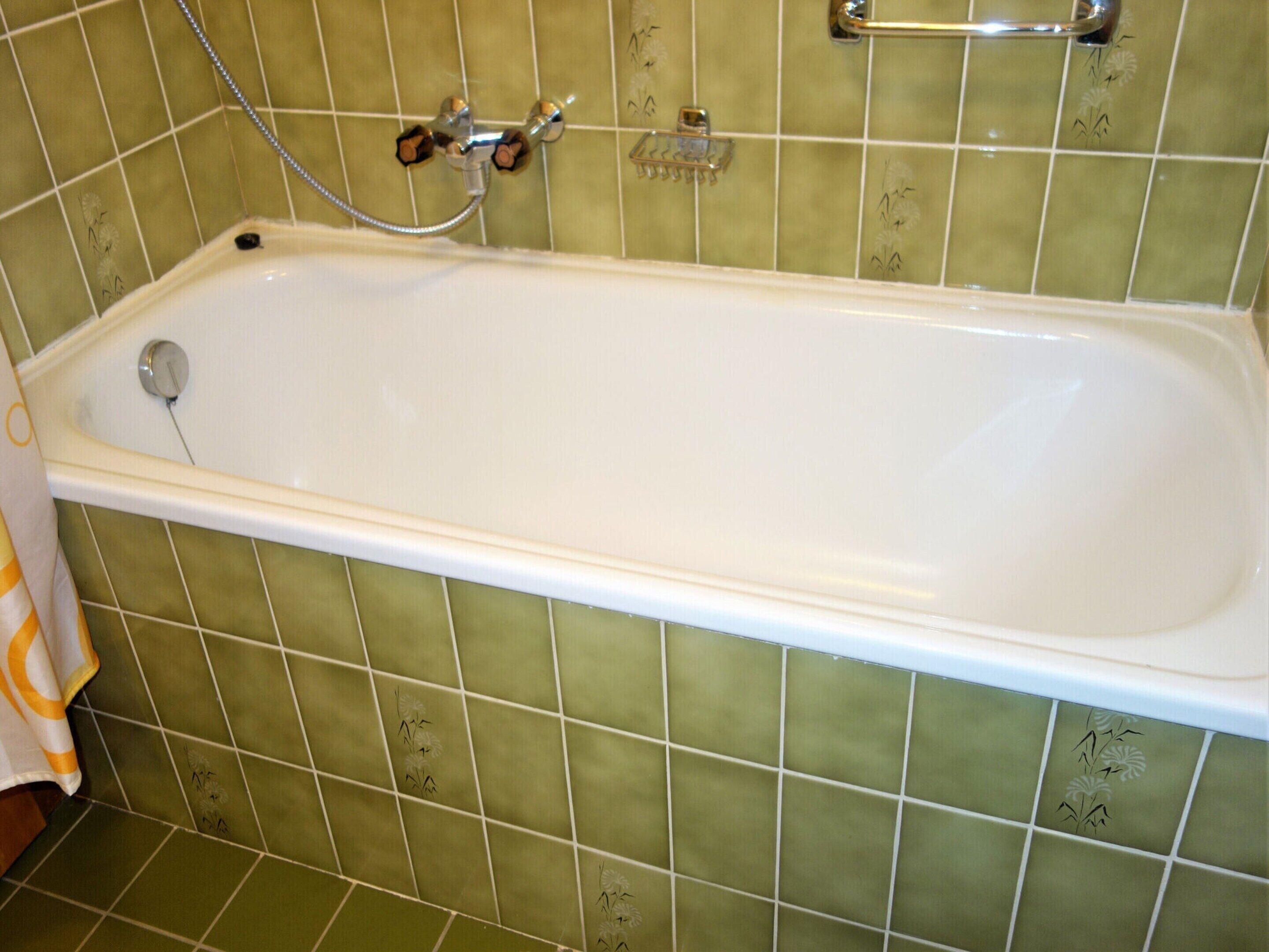 A bathroom with a bathtub, green tiled walls, and a showerhead.