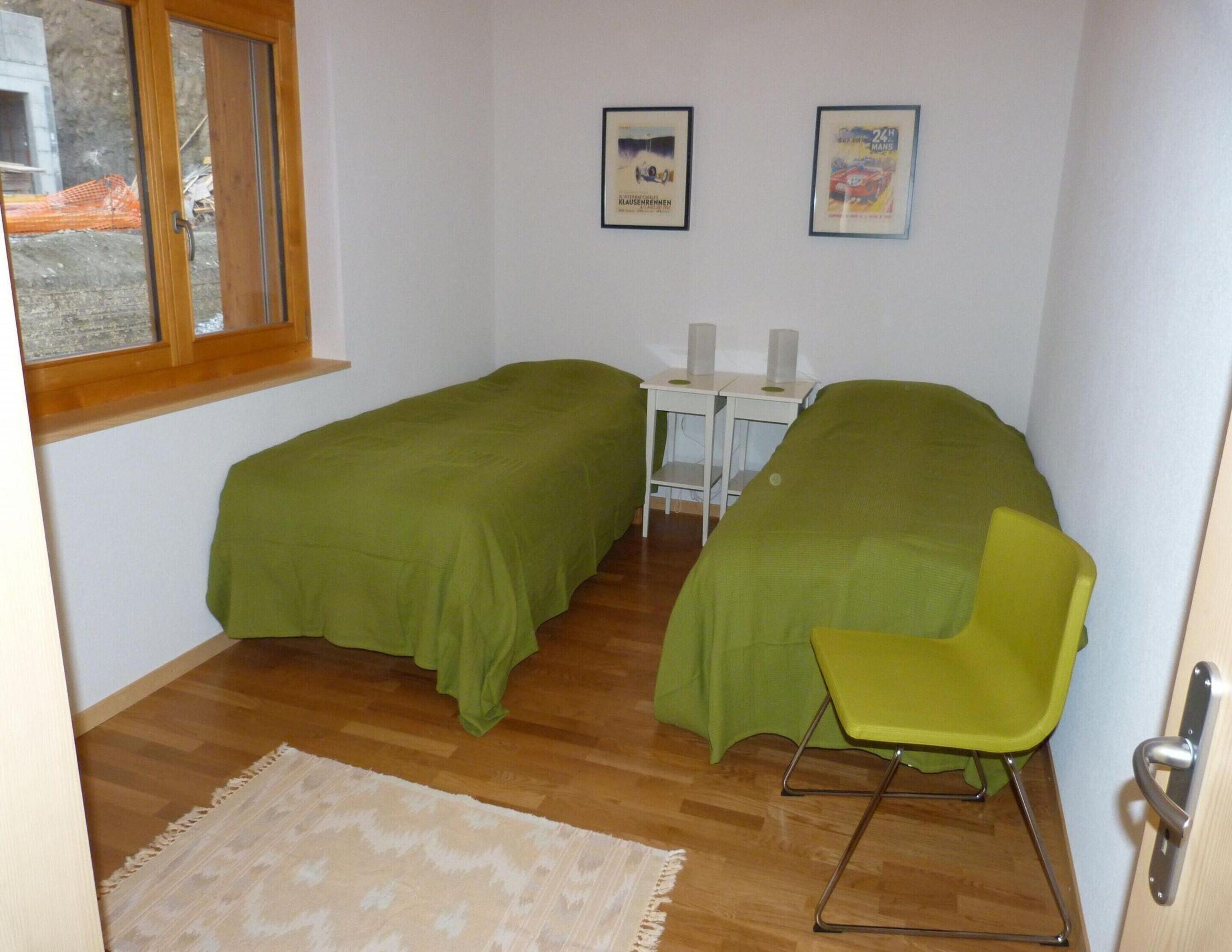 A small, tidy room with two single beds, a desk with a chair, and a window.