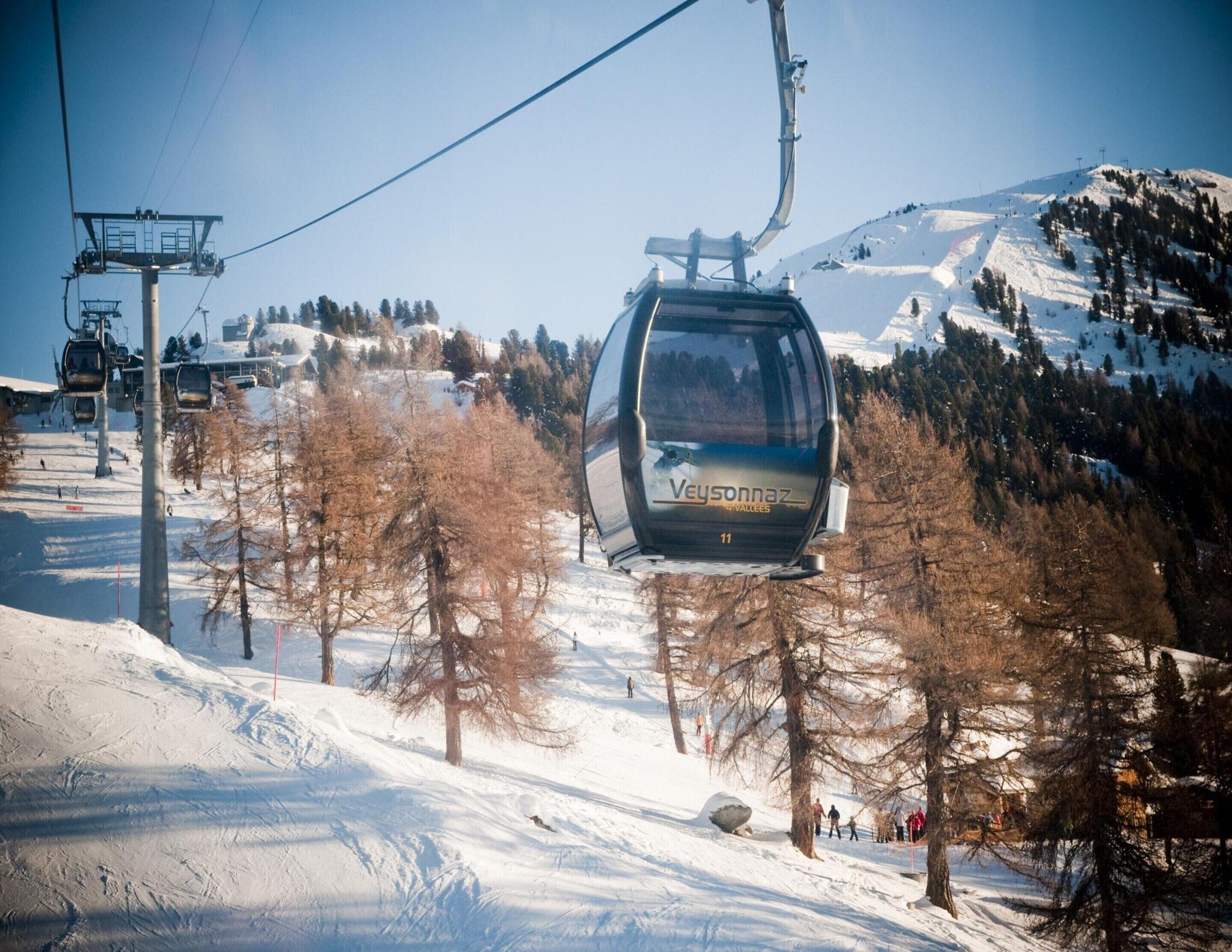 A cable car with "Veysonnaz" written on it, moving along a snowy mountain path with trees and other cable cars in the background.
