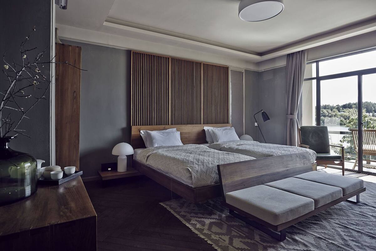 A modern bedroom with a large bed, bedside tables, a bench, and a view of a lake.