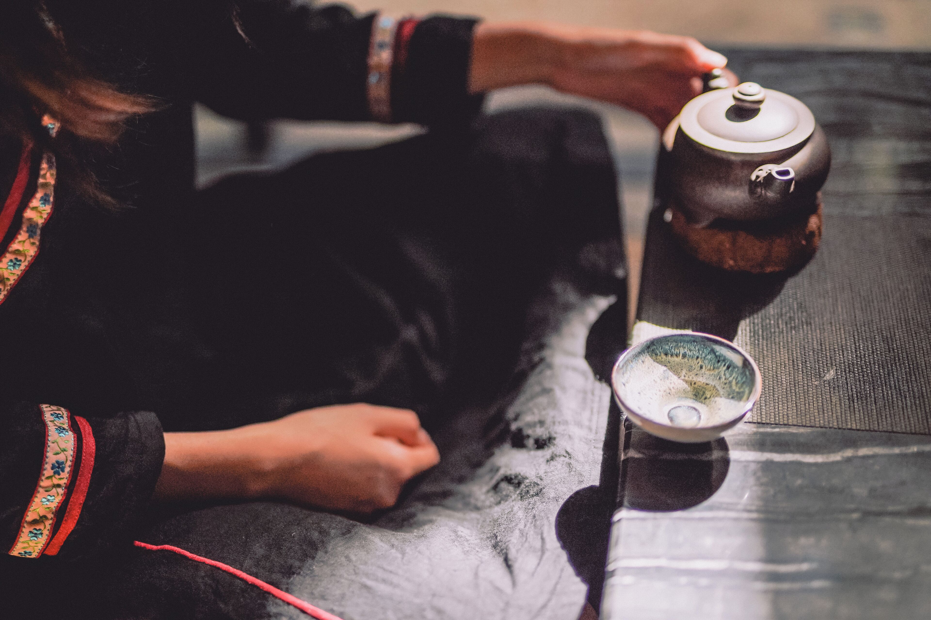 Una persona sentada en un sofá, con una tetera y una taza sobre una mesa.
