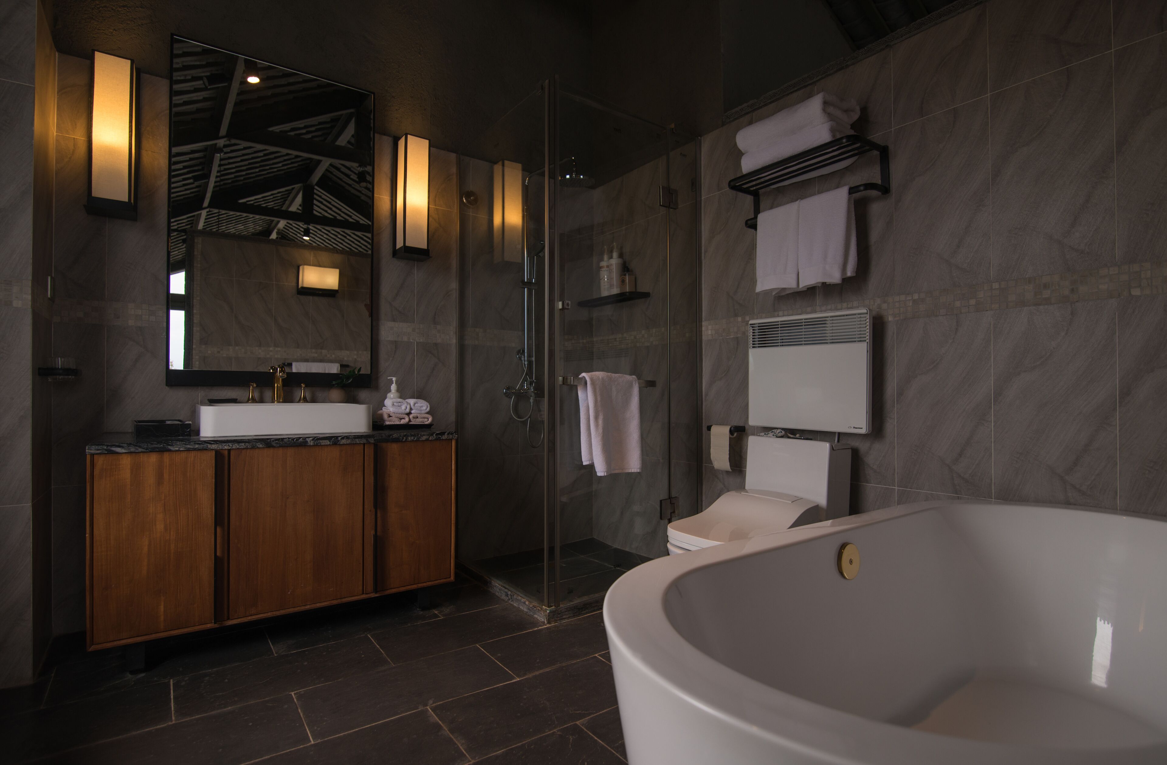 Een moderne badkamer met een vrijstaand bad, een douche met glazen wanden en een wastafel met spiegel en verlichting.