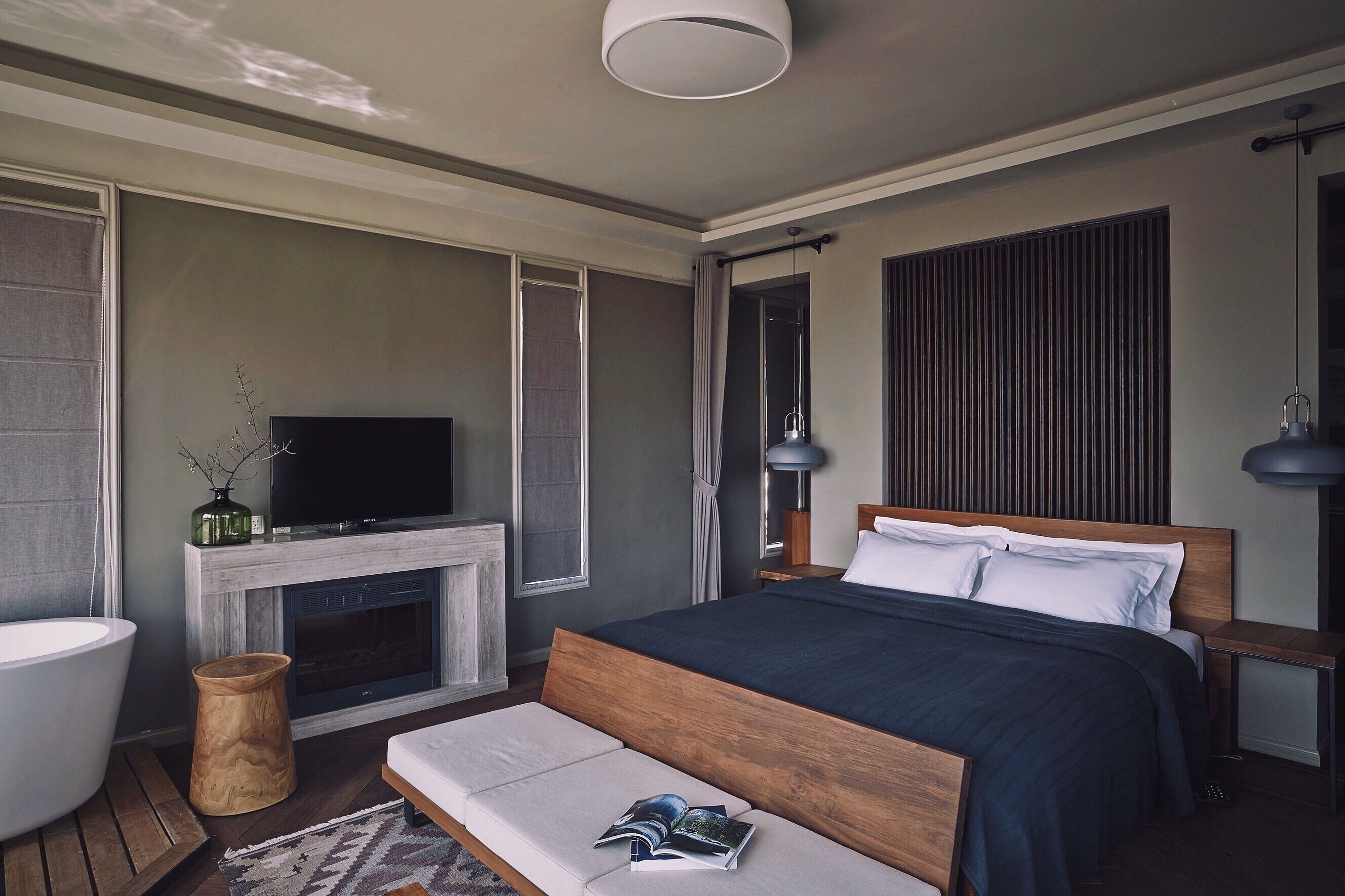 A modern bedroom with a large bed, a TV, a fireplace, and a wooden bench.